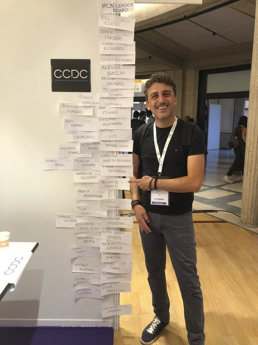 Someone standing next to and pointing at the CSD-Leaderboard at ECM33.