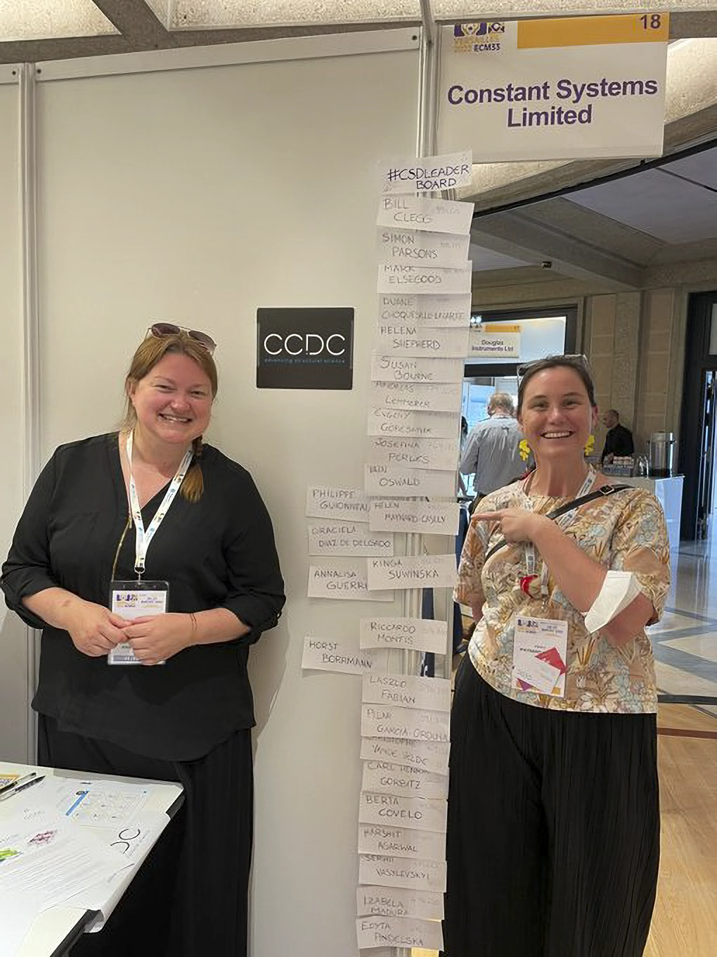 Someone standing next to and pointing at their name on the CSD-Leaderboard at ECM33.