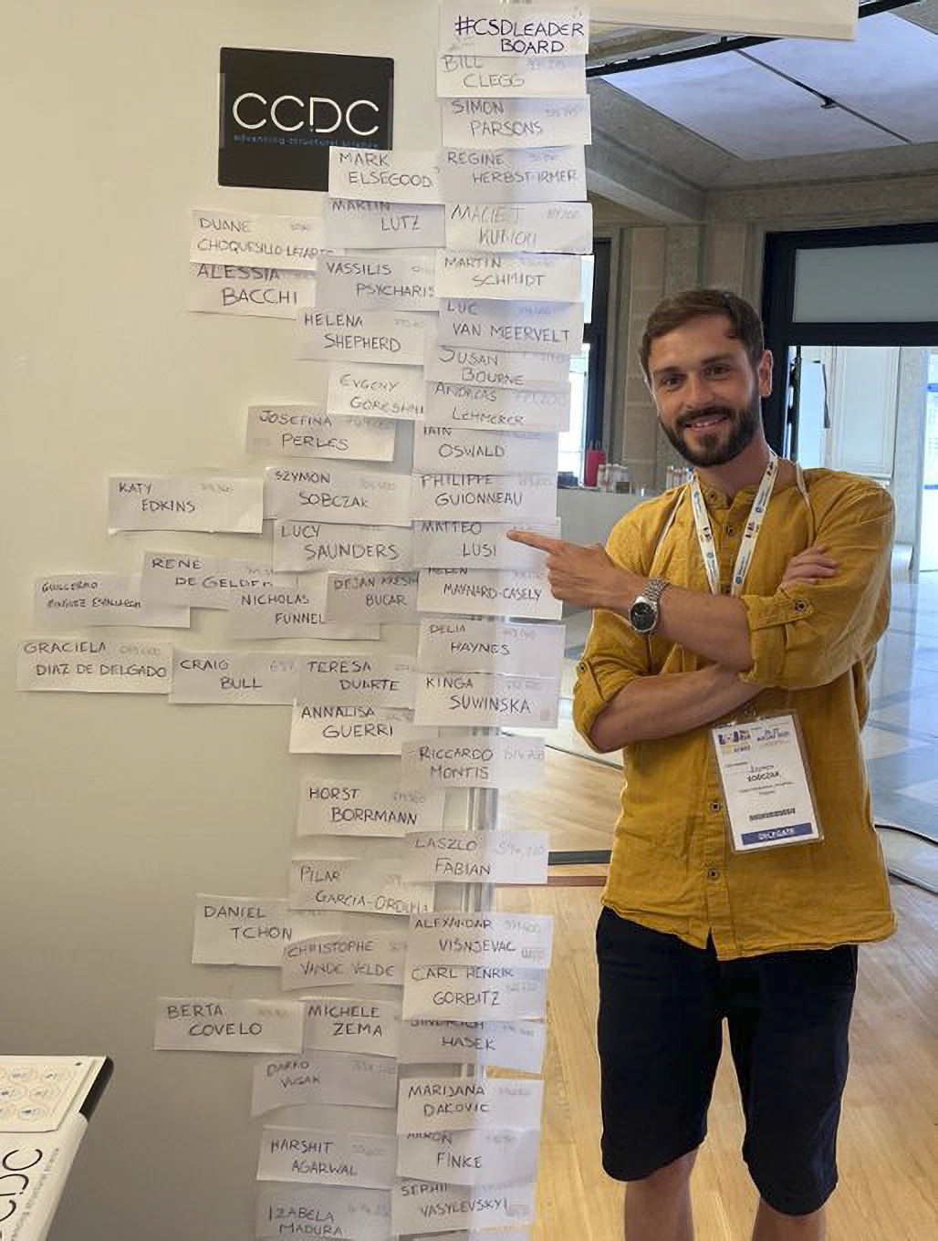 Someone standing next to and pointing at their name on the CSD-Leaderboard at ECM33.