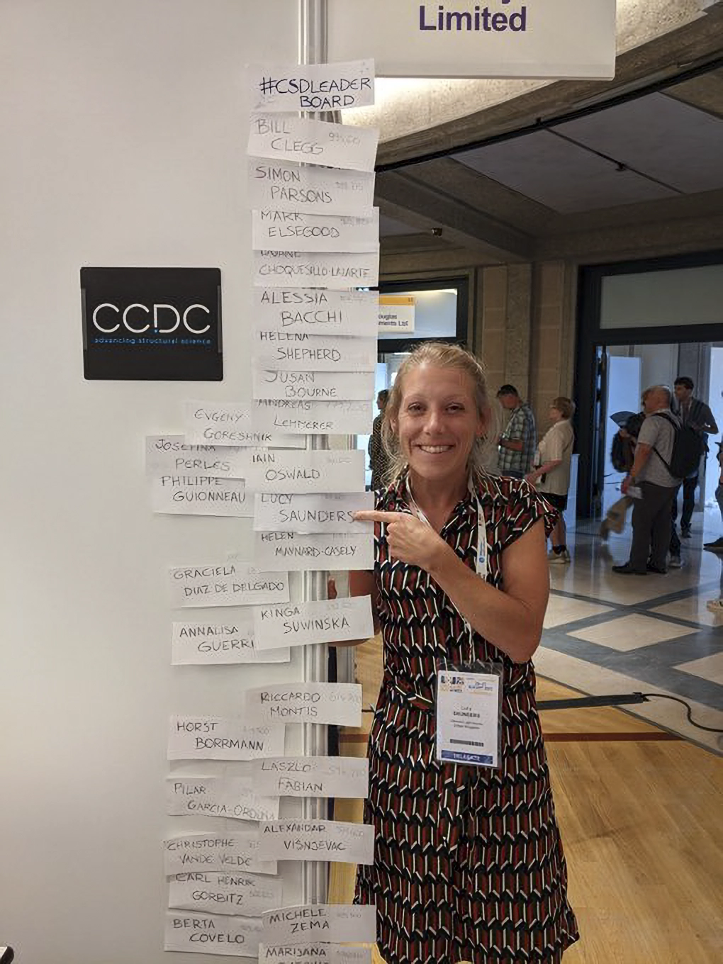 Someone standing next to and pointing at the CSD-Leaderboard at ECM33.