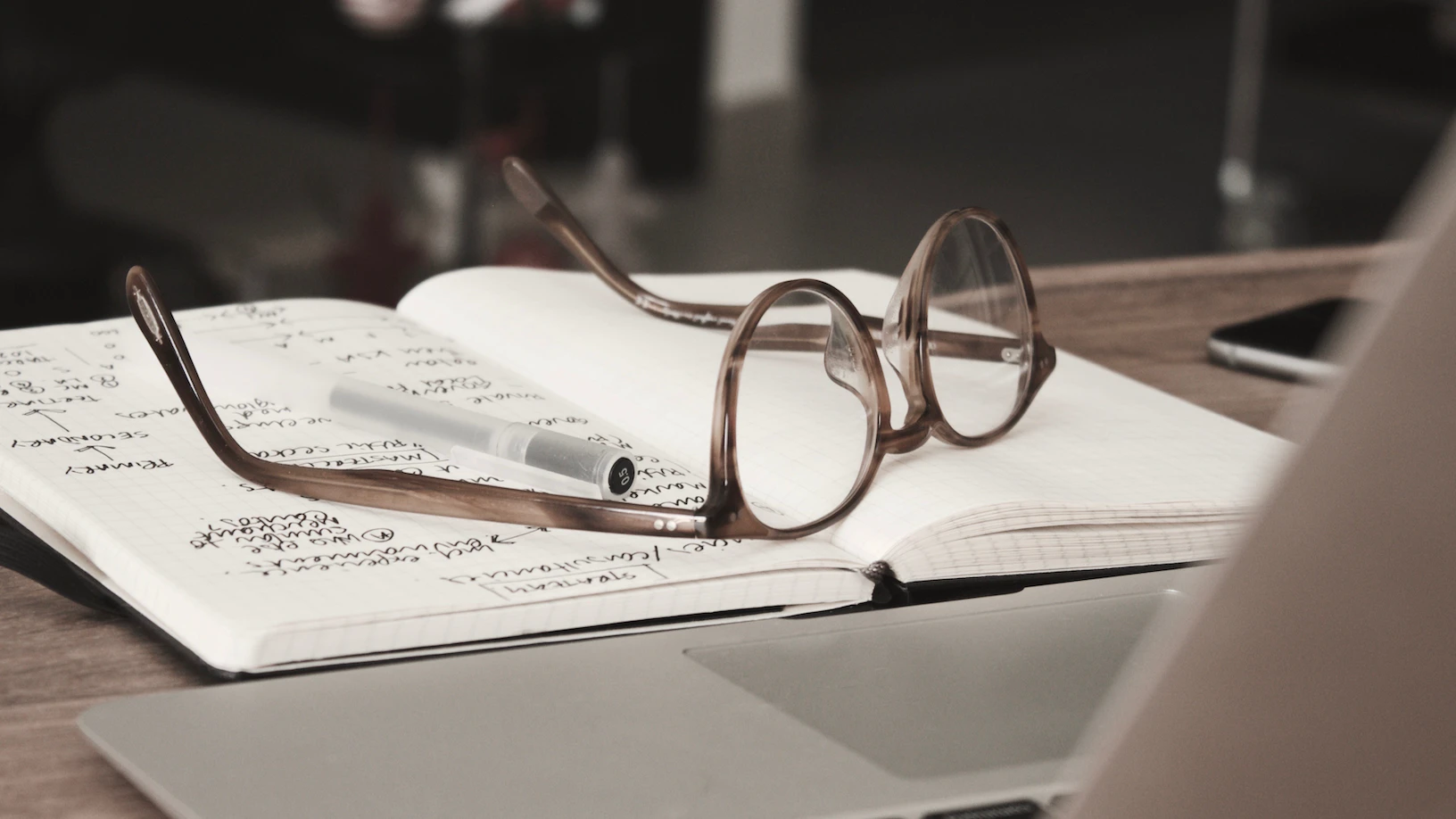 An open notebook with a pen and glasses.